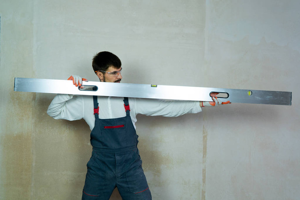 builder holds construction ruler with empty wall on background - Фото, зображення