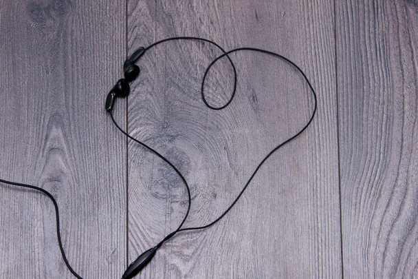 Earphones in shape or heart on wooden background. Flat lay, copy space. - Photo, Image