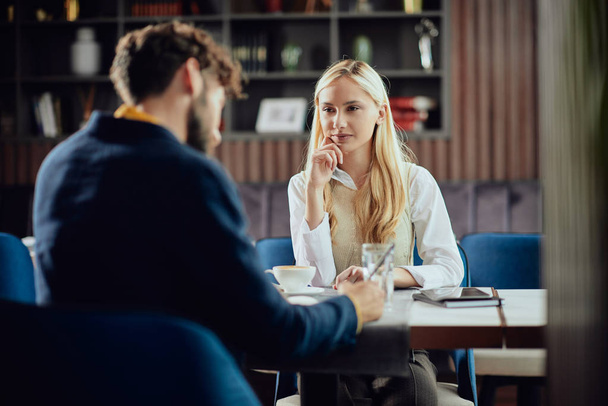Smiling Caucasian blonde businesswoman dressed smart casual discussing with her male colleague about project while sitting in coffe shop. - 写真・画像