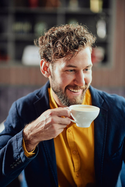 Portrait of young modern Caucasian man dressed smart casual sitting in cafeteria and drinking fresh coffee. - Foto, imagen