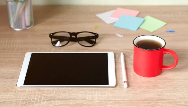 Wooden Desk. White tablet with black-rimmed glasses. Cup of tea. - Photo, image
