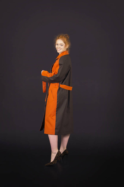 Beautiful, red-haired girl in an orange cloak posing. - Photo, image