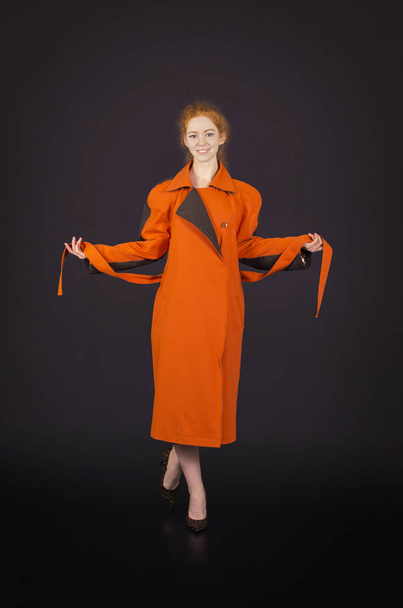Beautiful, red-haired girl in an orange cloak posing. - Фото, изображение
