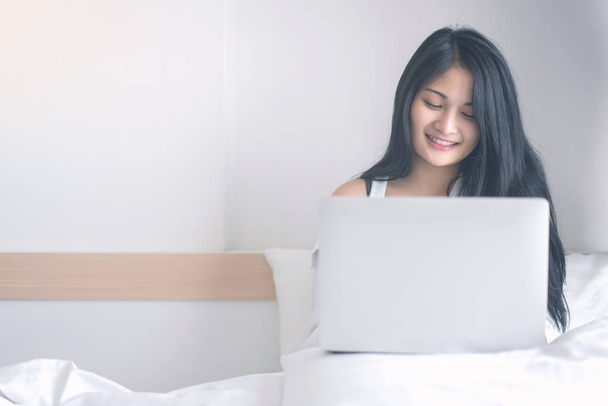 Young woman working on a laptop sitting on bed at home - Photo, Image