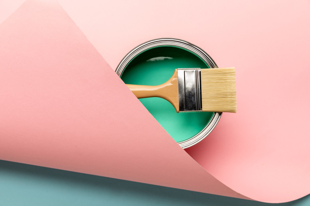 top view of tin of green paint and brush on pink surface - Фото, изображение