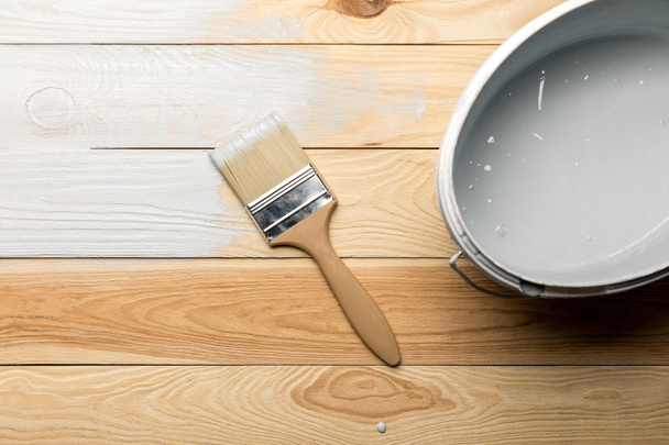 top view of brush and bucket of white paint on wooden surface - Foto, Imagen