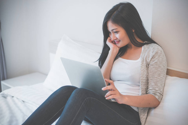 Dizüstü bilgisayarda çalışan genç bir kadın evde yatağında oturuyor. - Fotoğraf, Görsel