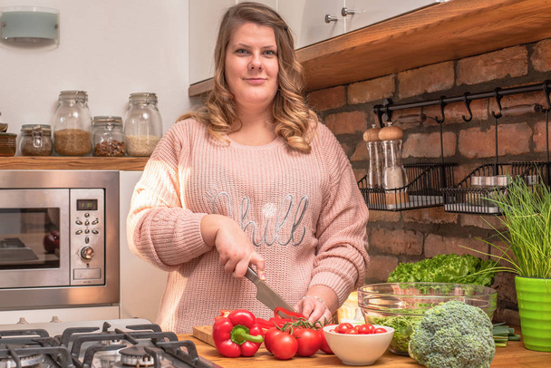 Hermosa mujer de tamaño grande está haciendo ensalada fresca en la cocina
 - Foto, Imagen