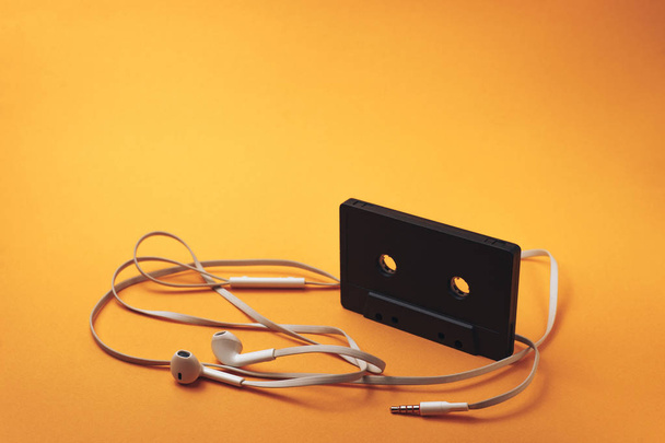 Czarna klasyczna magnetyczna taśma magnetofonowa i białe słuchawki na pomarańczowym tle. - Zdjęcie, obraz