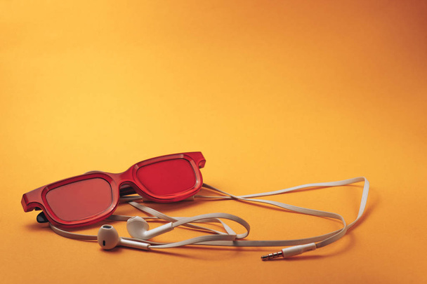 Червоні окуляри та білі навушники на помаранчевому фоні
. - Фото, зображення