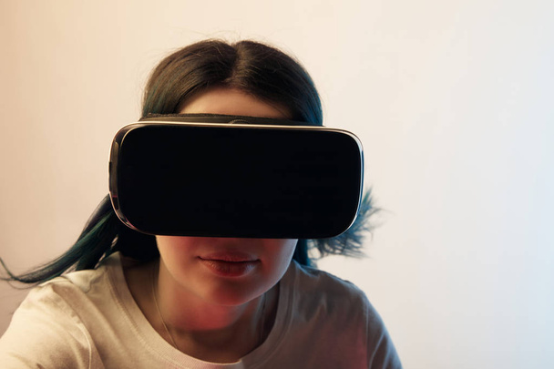 brünettes Mädchen mit Virtual-Reality-Headset und Blick in die Kamera auf beige  - Foto, Bild