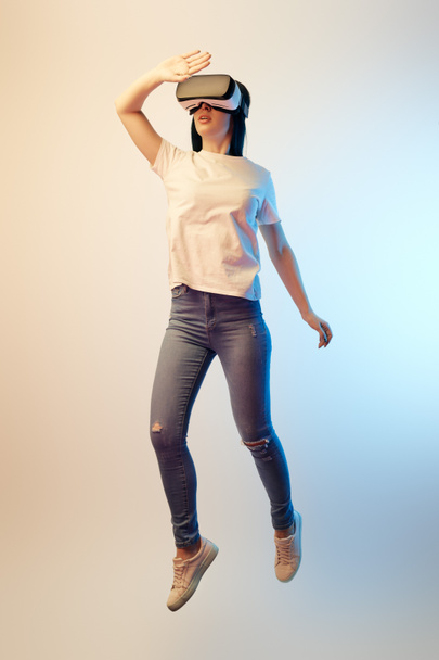brunette young woman in virtual reality headset levitating and gesturing on beige and blue  - Foto, Imagem