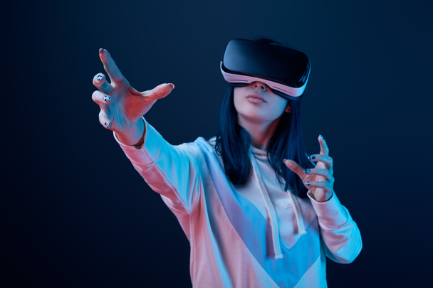 selective focus of young woman wearing virtual reality headset and gesturing on blue  - 写真・画像