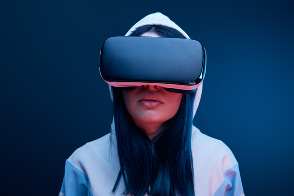 brunette girl in hood wearing virtual reality headset on blue - Photo, Image
