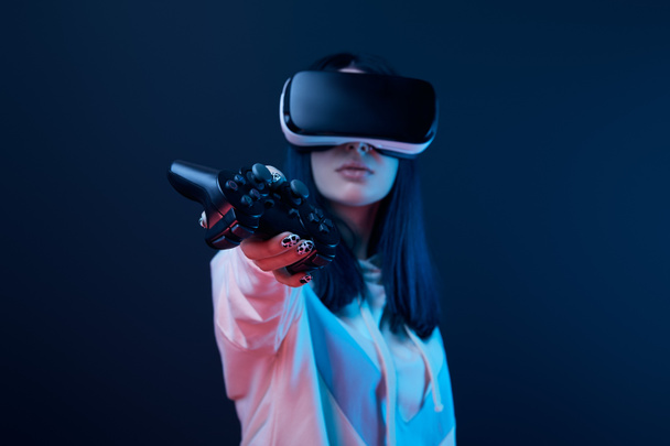 KYIV, UKRAINE - APRIL 5, 2019: Selective focus of young woman holding joystick while using virtual reality headset on blue  - Фото, изображение
