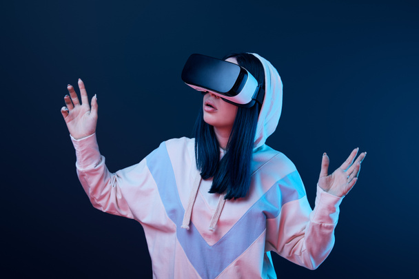 mujer morena sorprendida haciendo gestos mientras usa auriculares de realidad virtual en azul
  - Foto, Imagen