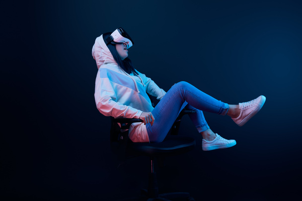 donna sorpresa utilizzando auricolare realtà virtuale mentre seduto sulla sedia blu
  - Foto, immagini