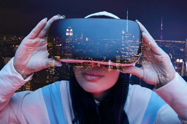 kettős expozíció barna lány megható virtuális valóság headset és a modern város felhőkarcolók az éjszakai  - Fotó, kép