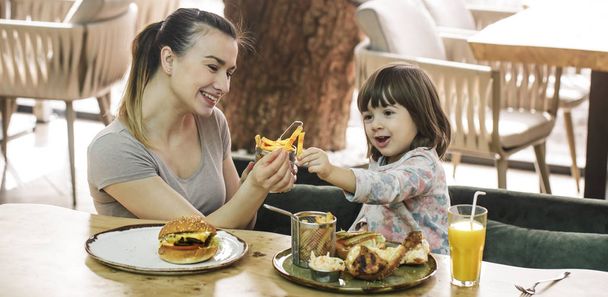 Mamá con una linda hija comiendo comida rápida en un café
 - Foto, Imagen