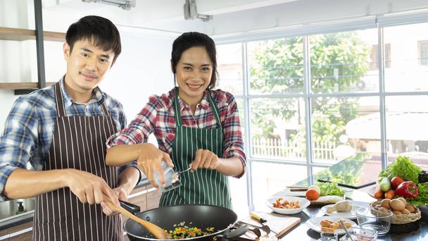 Νεαρό ζευγάρι ασιατών είναι στην ευχάριστη θέση να μαγειρέψουν μαζί, δύο οικογένειες βοηθούν ο ένας τον άλλον να προετοιμαστούν για να μαγειρέψουν στην κουζίνα. - Φωτογραφία, εικόνα