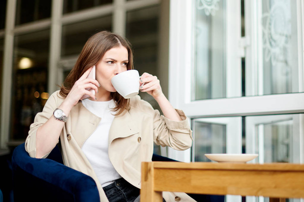 Νεαρή γυναίκα στο καφέ με τηλέφωνο και καφέ - Φωτογραφία, εικόνα