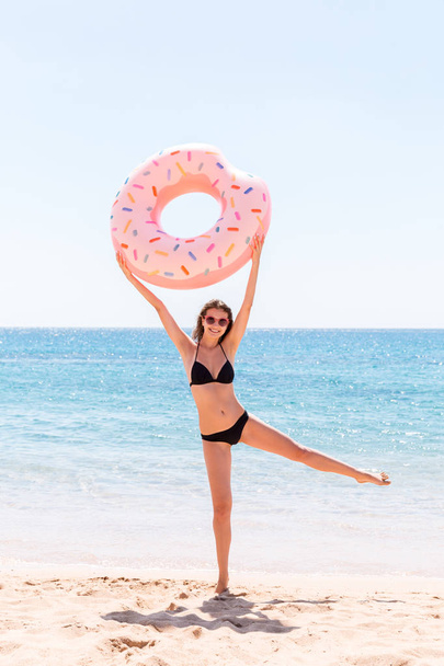 Enjoying suntan. Beautiful crazy woman relaxing and playing with inflatable ring in sea beach. Summer holidays and vacation concept - Photo, Image
