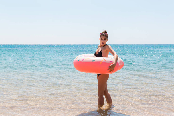 Woman relaxing with inflatable ring on the beach. shocked or surprised girl in the cold sea. Summer holidays and vacation concept - Photo, Image