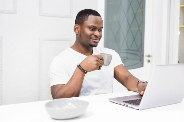 Young African American businessman working on a laptop in the kitchen in a modern interior. - Fotó, kép