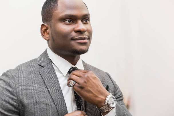Young African American businessman in a gray suit tying a tie on a white background. - Foto, Imagem