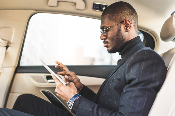 Young businessman using tablet while sitting in the backseat of a car. - Foto, immagini