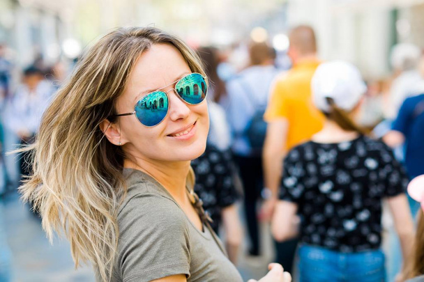 Smiling woman in sun glasses looking back in a city. - Foto, Imagen