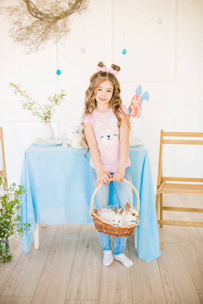 Little cute girl with long curly hair with little bunnies and Easter decor at home at the holiday table. - Foto, Imagem