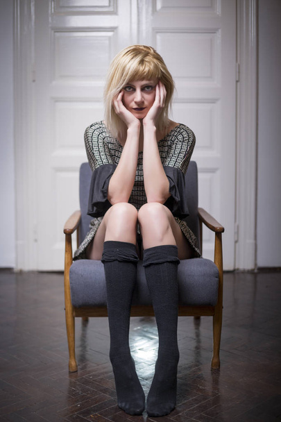 Kaunis nuori blondi nainen päällään rento mekko istuu tuolissa
 - Valokuva, kuva