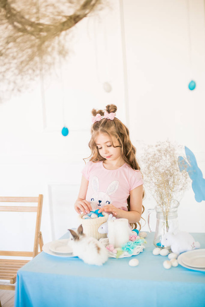 Little cute girl with long curly hair with little bunnies and Easter decor at home at the holiday table. - Valokuva, kuva