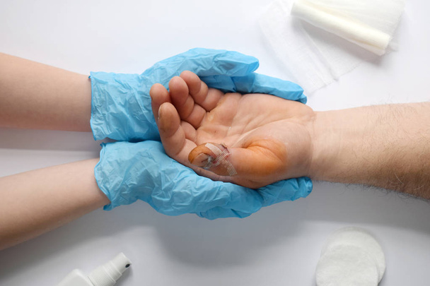 Lekarze ręce trzyma męską rękę z krwawe Gash na dużym palcu. Lekarz bada pacjenta. Cierpliwy doping i wsparcie. Leczenie ran środkiem antyseptycznym. - Zdjęcie, obraz