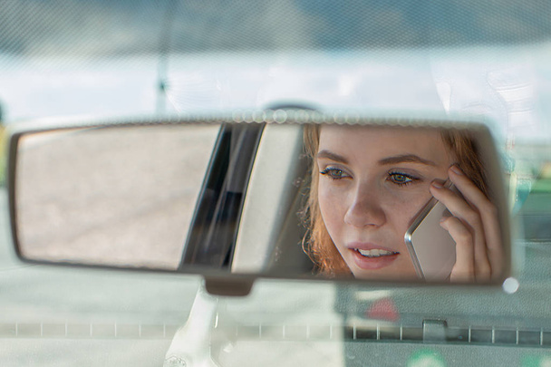 Young woman drives a car and talks on the phone - Фото, изображение