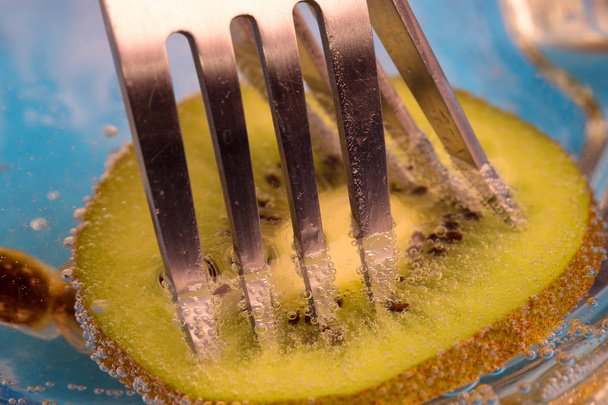 metalen vorken vast in groene kiwi alle onder water, bubbels op fruit en vorken - Foto, afbeelding