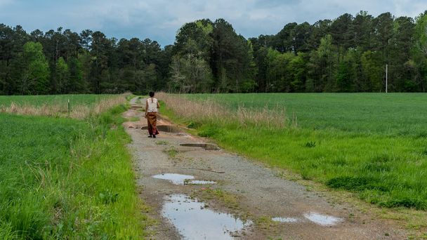 Frau in Sarong läuft auf Feldweg mit Pfützen im Feld - Foto, Bild
