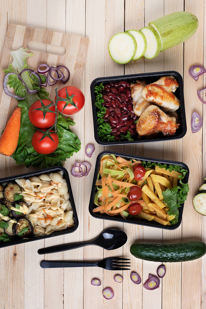 Blick von oben auf gesundes Mittagessen zum Mitnehmen. Hühnerkeulen, Bohnen, Pommes, Salat, Nudeln  - Foto, Bild