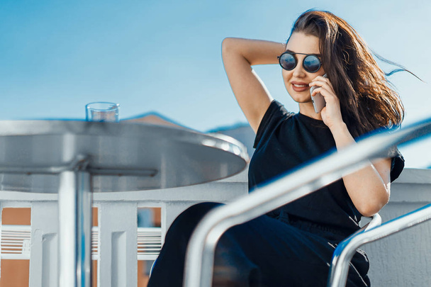 Stylish young woman sitting outdoors on balcony and talking by mobile phone. - Foto, immagini