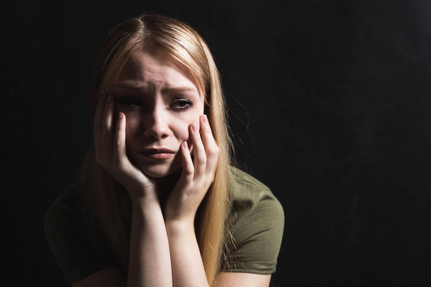 Sad young woman going to cry in a black background - Foto, Imagen