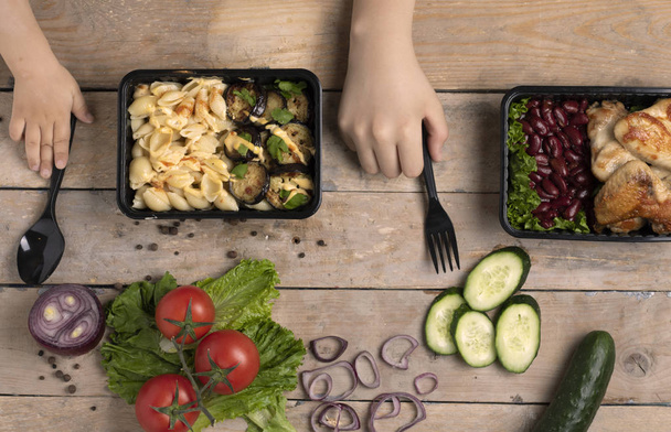 wegańskie jedzenie w czarnych plastikowych pojemnikach, gotowy posiłek do jedzenia i dzieci ręce, widok z góry - Zdjęcie, obraz