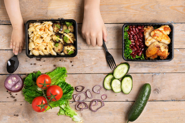 Veganes Essen in schwarzen Plastikdosen und Kinderhänden, Fertiggerichte und Kinderhände, Ansicht von oben - Foto, Bild