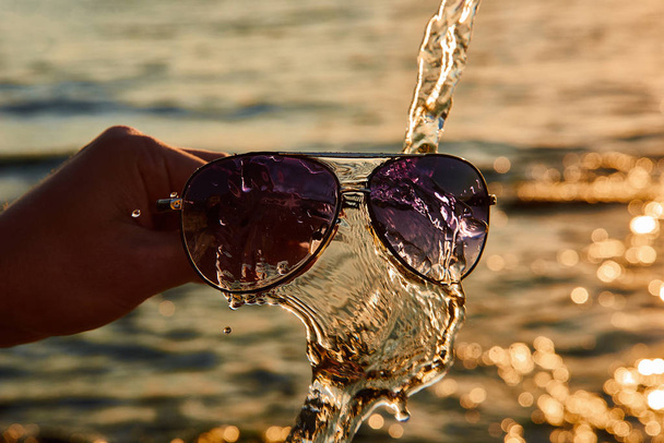 Μια ακτίνα ήλιου λάμπει στο ποτήρι των γυαλιών, σκίαση από σταγόνες νερού. σταγόνες στα ποτήρια - Φωτογραφία, εικόνα