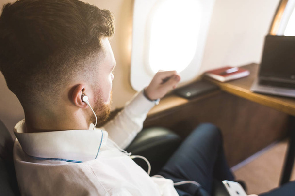 Young attractive and successful businessman is resting and listening to music works while sitting in the chair of his private business plane - Zdjęcie, obraz