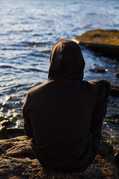 O homem está sentado à beira-mar a ver o pôr-do-sol. Homem triste sentado junto ao mar. Conceito sobre as pessoas, tristeza e solidão
 - Foto, Imagem