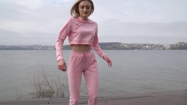 Happy young female dancer caucasian girl in pink urban street dancing freestyle in the city by the lake - Materiaali, video