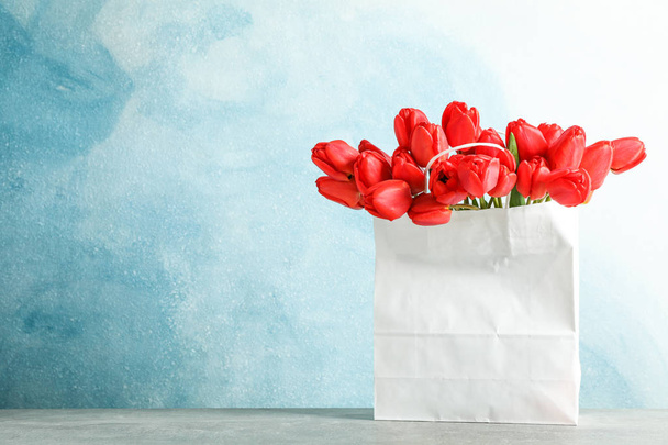 Papiertüte mit schönen roten Tulpen auf dem Tisch vor blauem Hintergrund - Foto, Bild