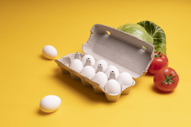 Chicken eggs in a tray and vegetables on a yellow background - Photo, Image