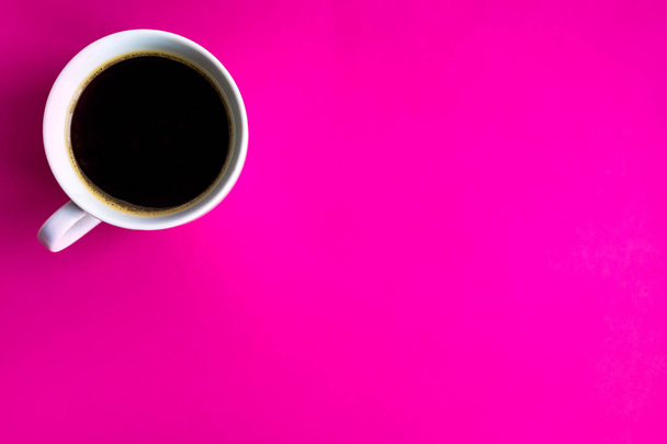 Een kopje koffie op een Felroze achtergrond. Een kopje met een koffie gefotografeerd vanaf de top en met een plaats voor kopieer ruimte. Koffie in de ochtend - Foto, afbeelding